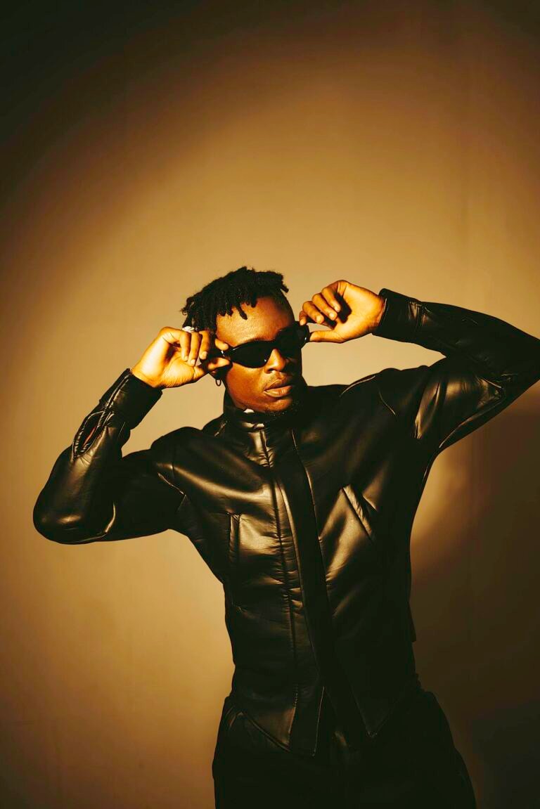Confident man in a leather jacket and sunglasses posing in a modern fashion shoot.