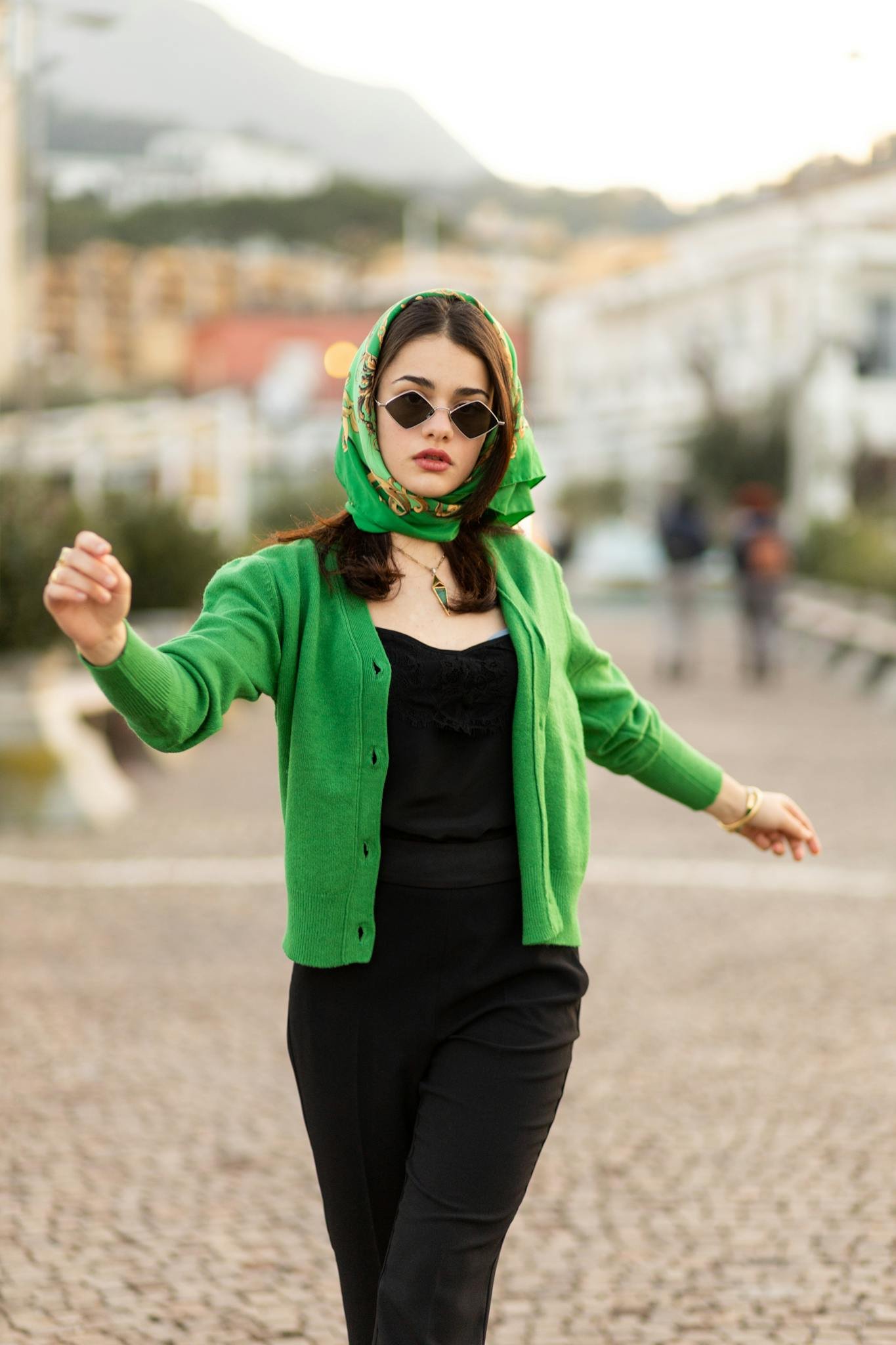 Stylish woman in green cardigan and sunglasses walks confidently outdoors, exuding elegance and fashion.